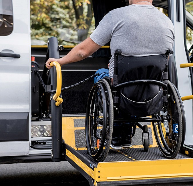 A man in a wheelchair using a hydraulic lift to board a white accessible van