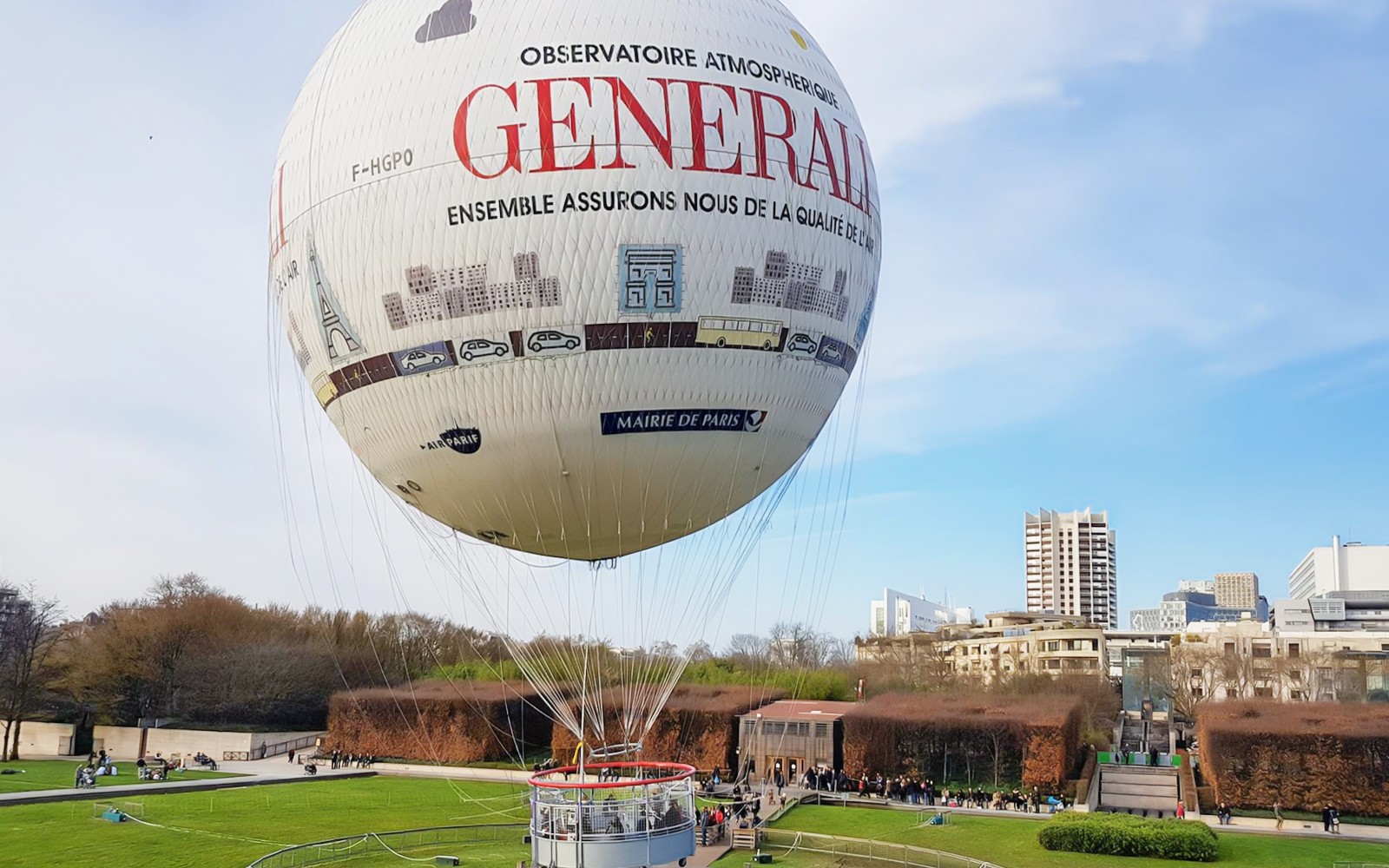 Ballon de Paris Generali được buộc tại một công viên với cảnh quan thành phố trong nền.