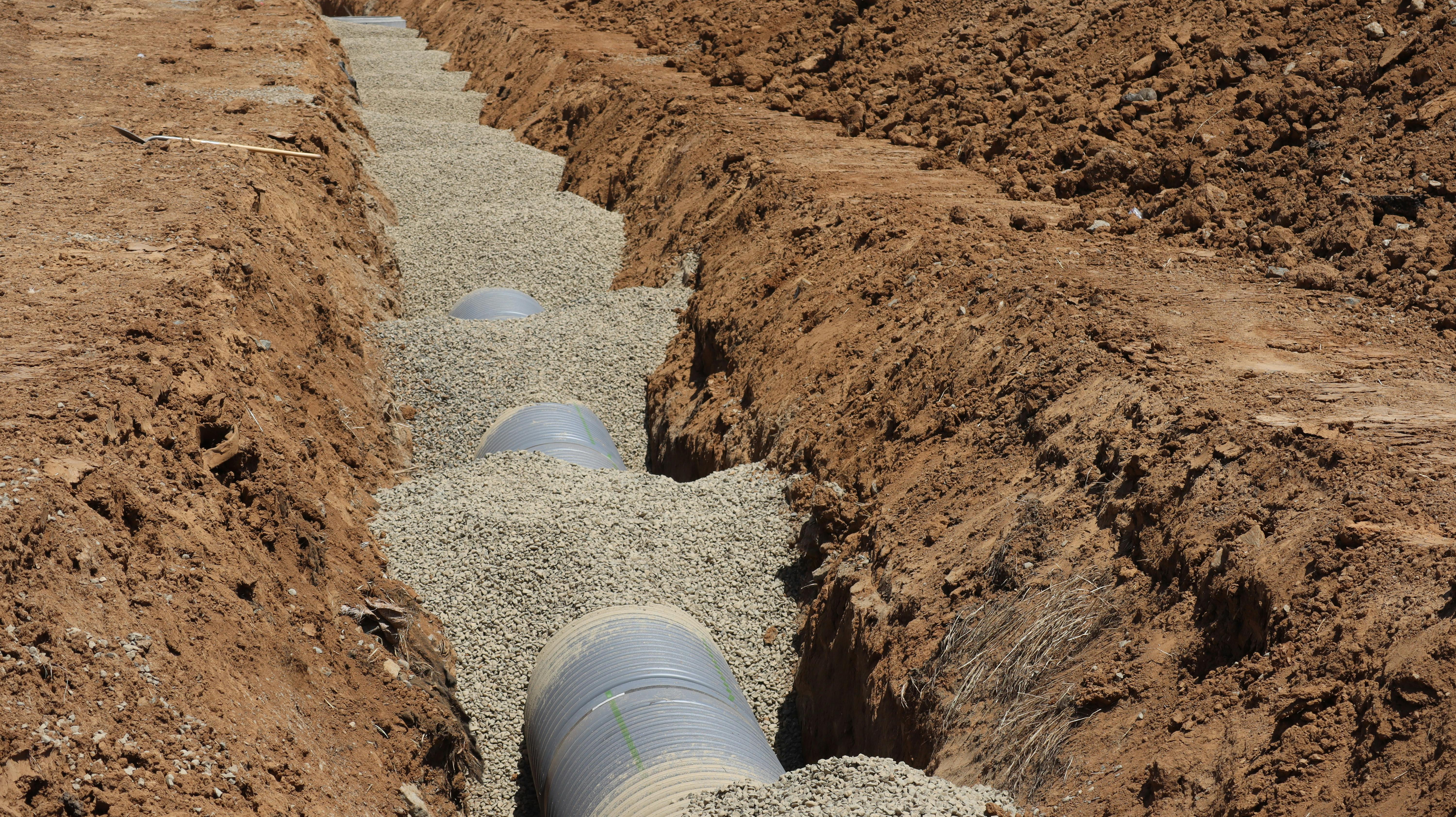 Pipe being installed in a freshly dug dirt trench.