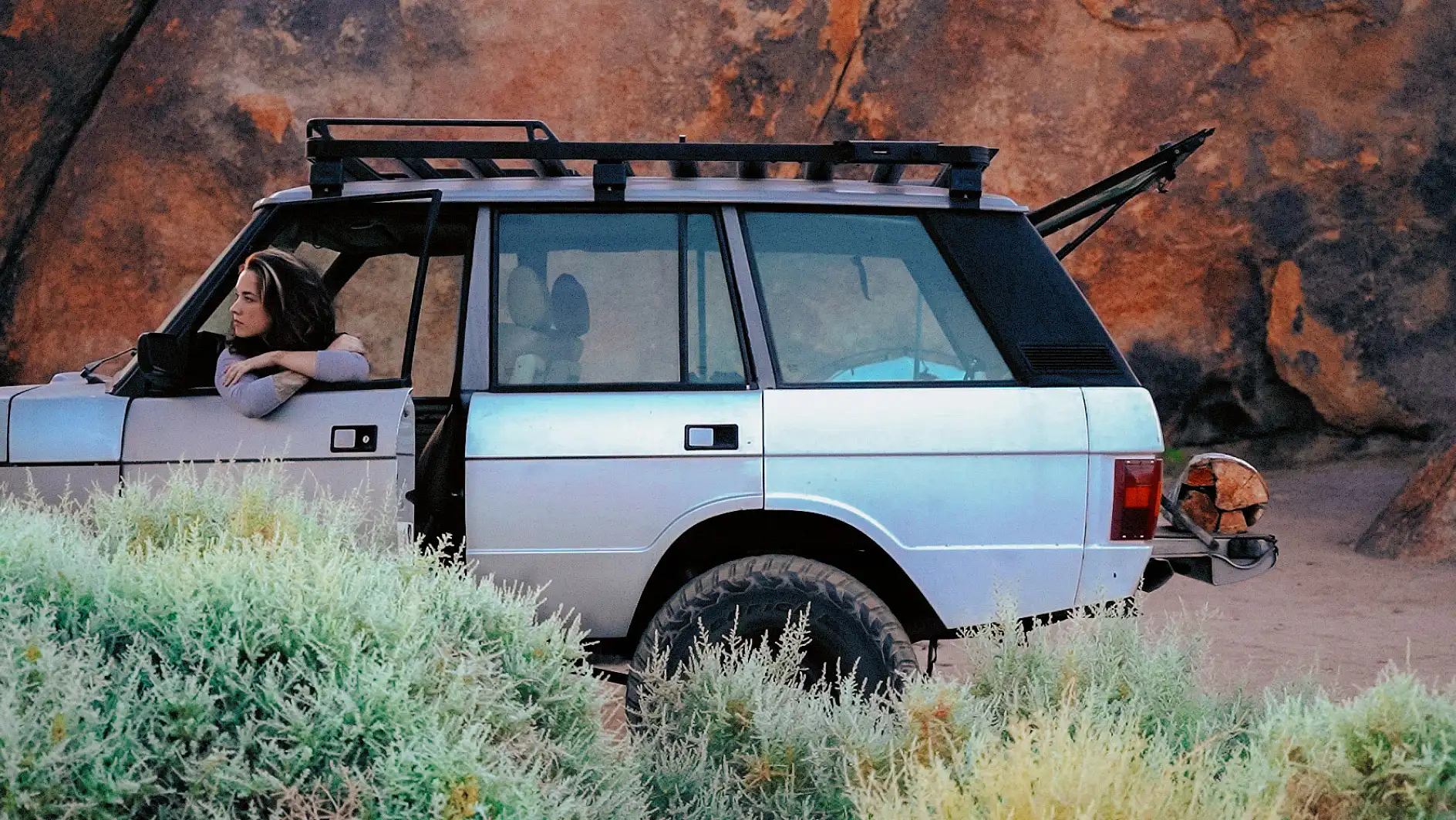 A woman leaning on the door of a Range Rover SUV.