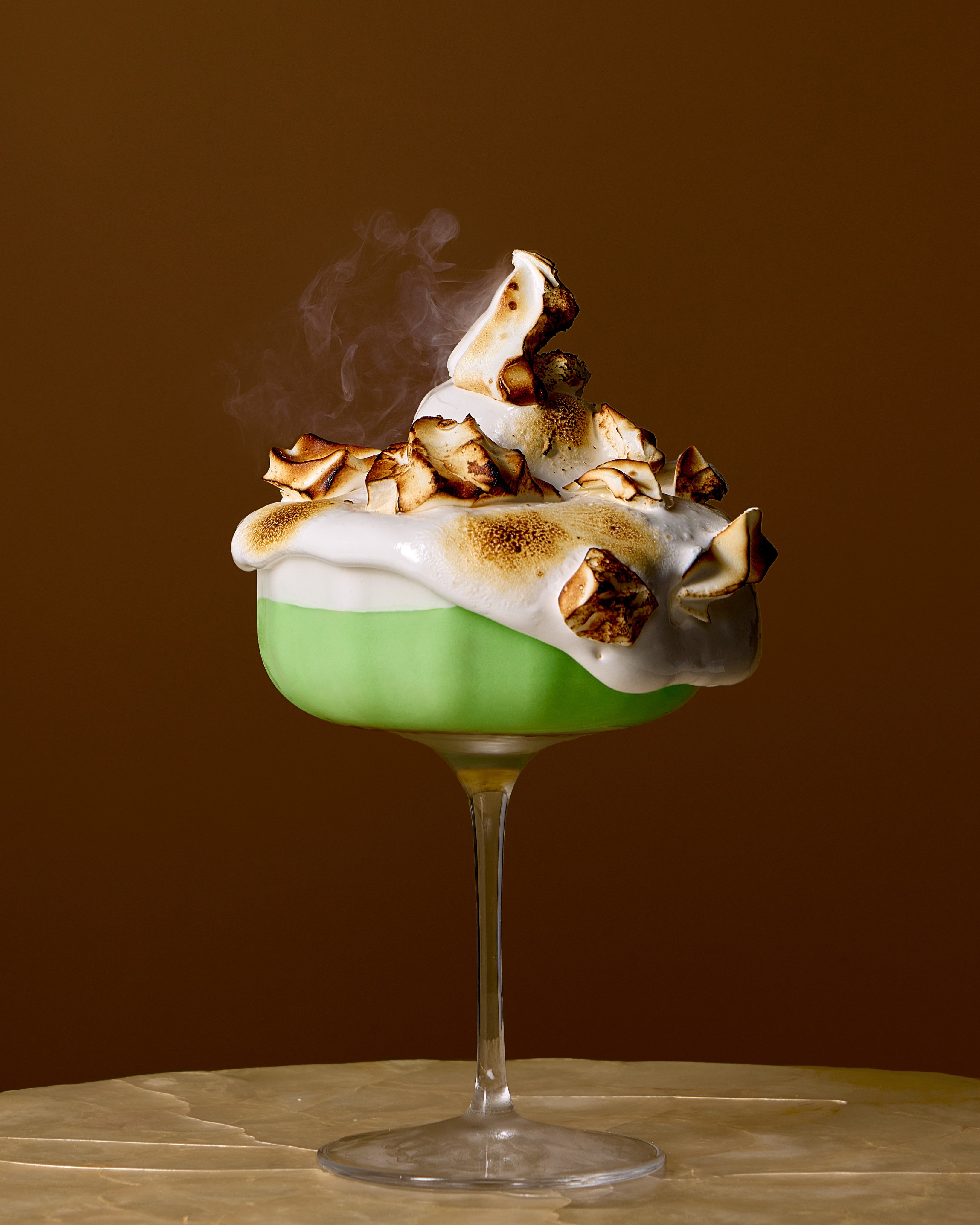 Green dessert coupe topped with toasted meringue and rising smoke