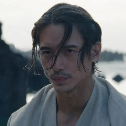 Qimir in a white robe on an island with his hair in his face