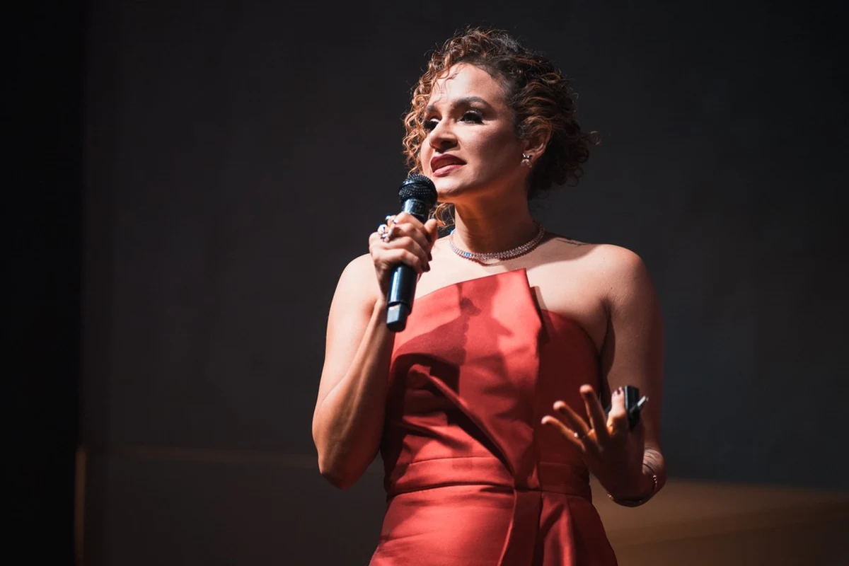 Ítala dos Anjos no palco, de vestido vermelho, falando ao microfone