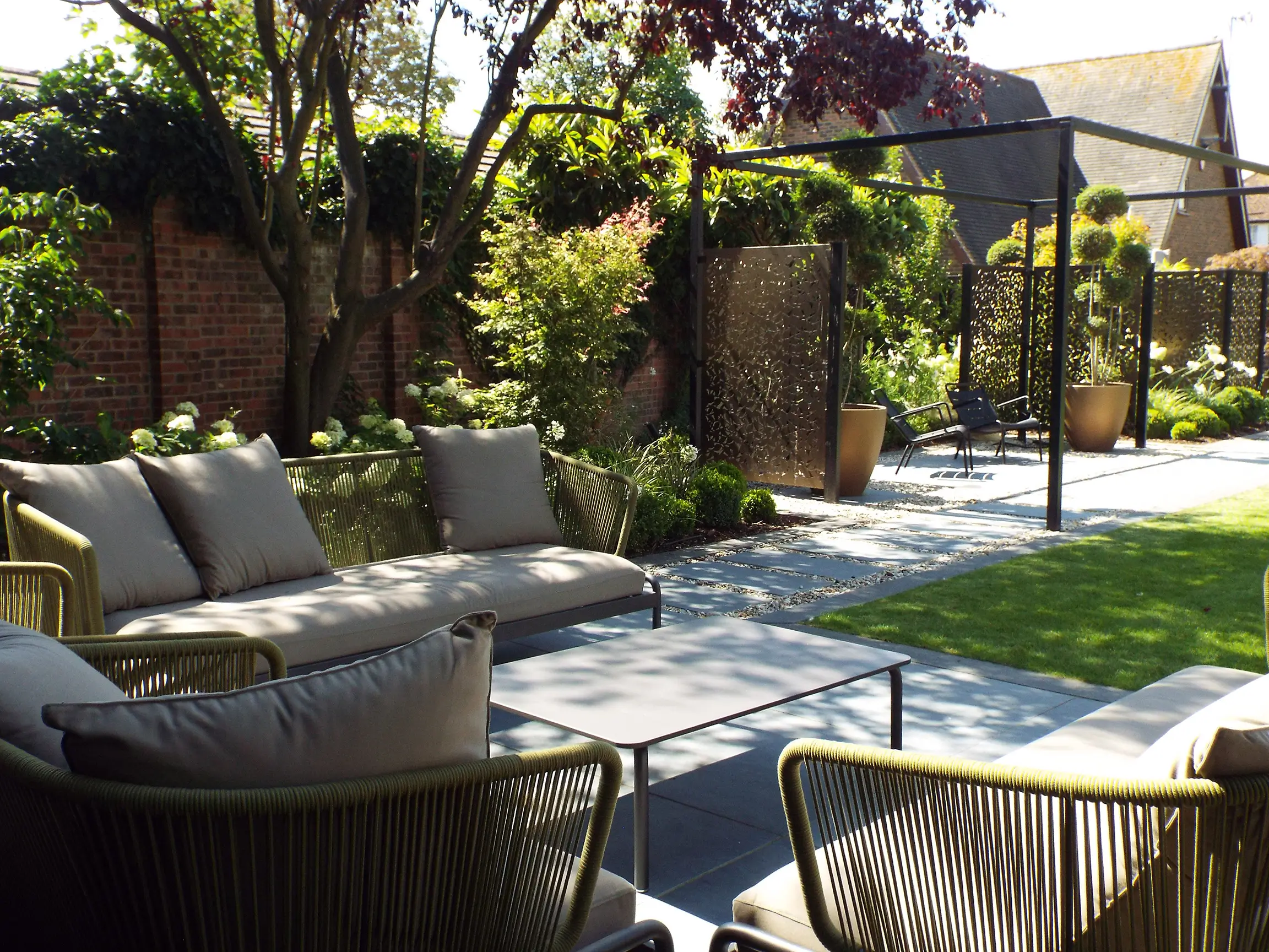 A serene garden with lounge chairs, greenery, and a sunny pathway leading through the tranquil space.