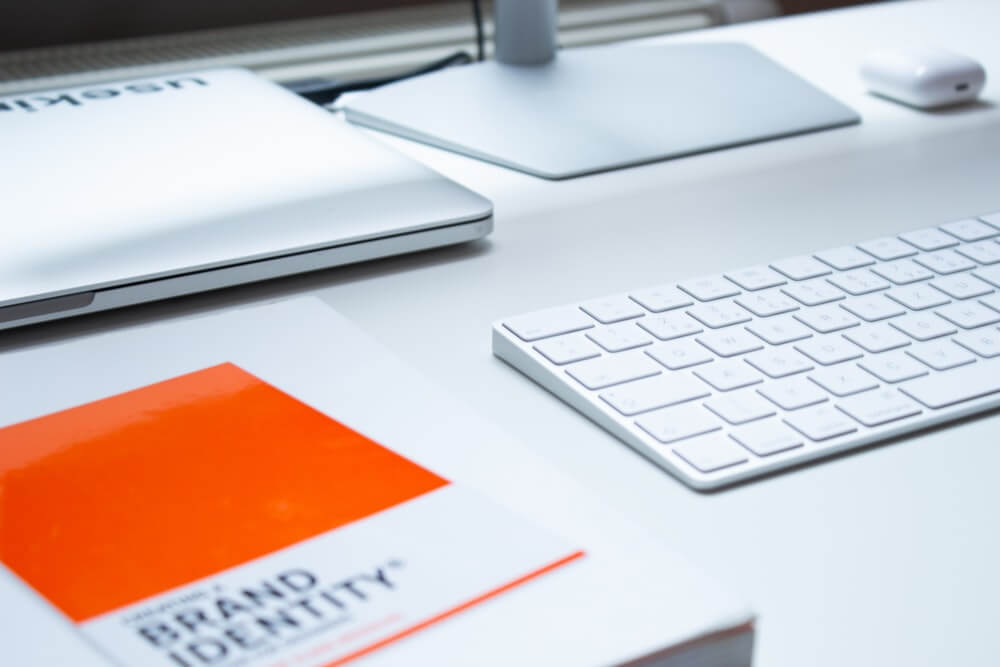 A desk with a laptop, a monitor,  keyboard and a book on top
