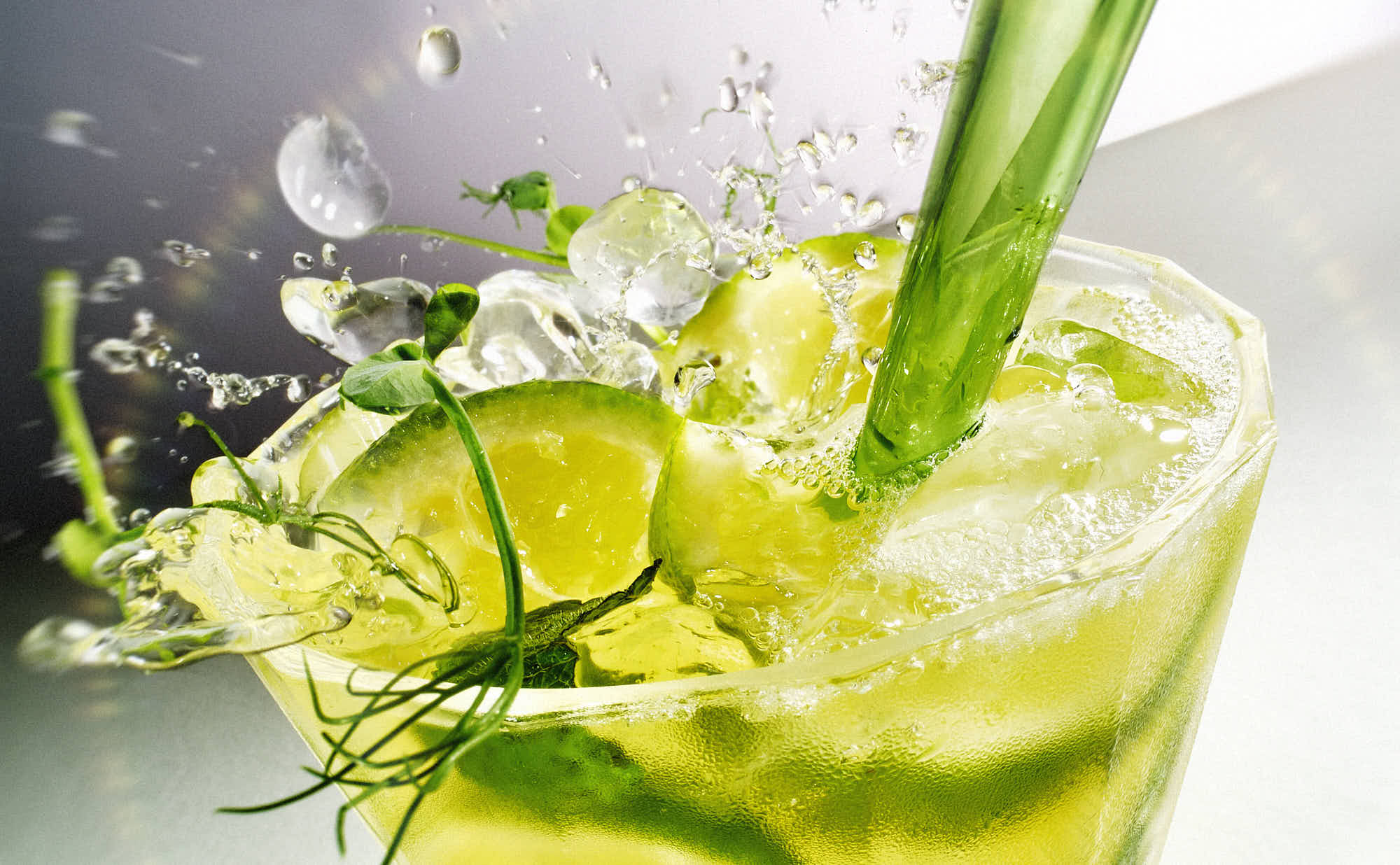 A refreshing drink with lime and mint leaves surrounded by splashes of water on a light background.