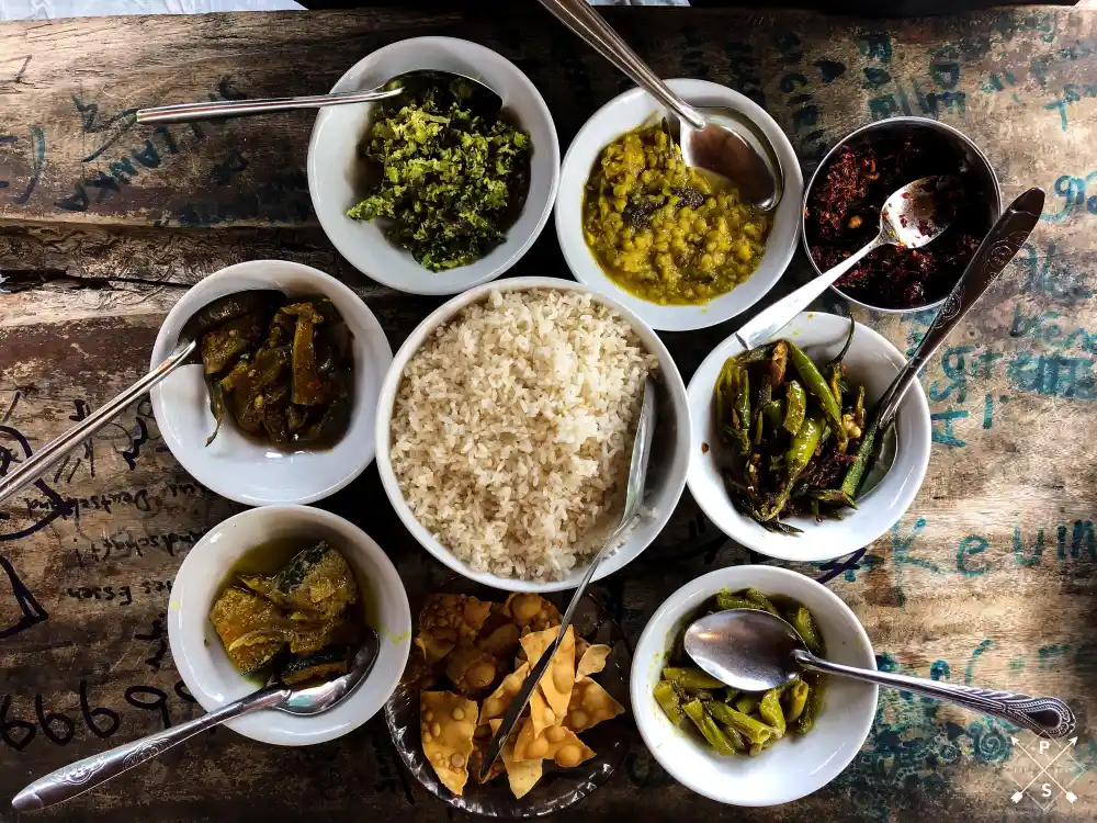 Traditional Kerala Ayurvedic meal served on a rustic table, featuring red rice, seasonal vegetable curries, lentils, stir-fried greens, and herbal preparations, representing an Ayurvedic seasonal diet (Ritucharya) followed for summer, monsoon, and winter wellness at Au Revoir Wellness Resort in Kerala.