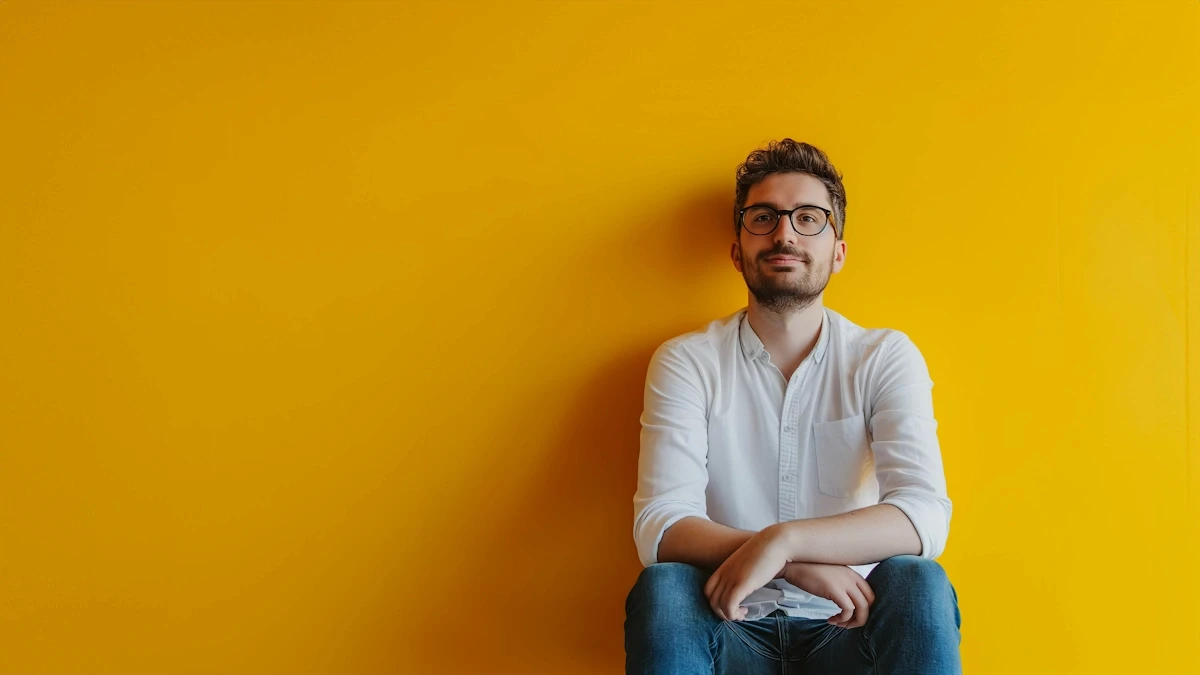 Caucasian man with glasses in white shirt and jeans against a vibrant yellow background, exuding a relaxed demeanor.