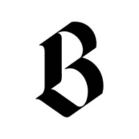 Person wearing a blue puffer jacket and red backpack standing in front of a light blue building on a city street.