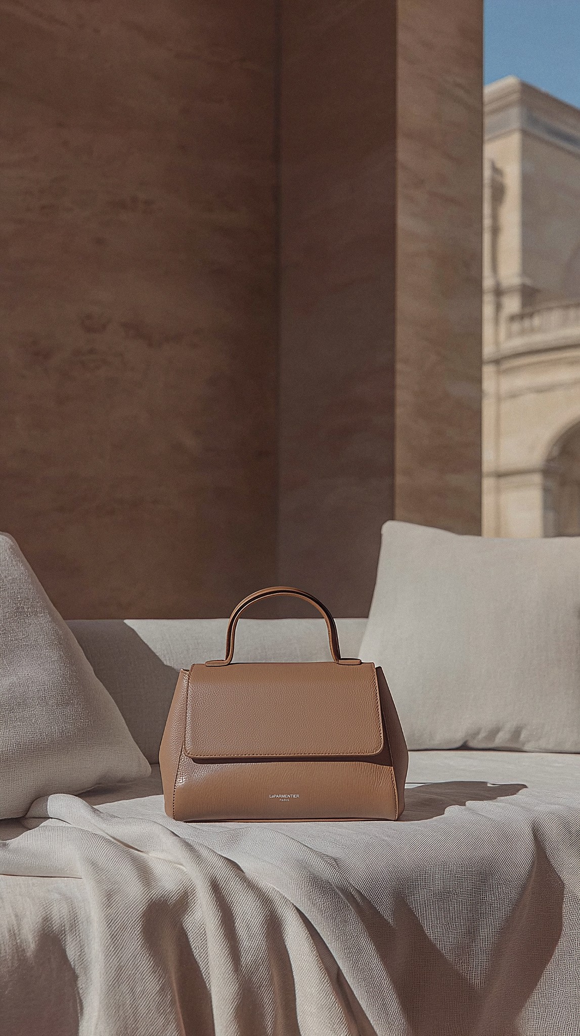 AI fashion visual of a woman in a minimalist beige blazer and dress holding a camel leather handbag, created by Myrovia Labs for LeParmentier. AI branding and product photography for luxury accessories.
