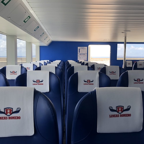 Interior of a ferry with rows of navy blue seats, each with a white cover displaying the "LINEAS ROMERO" logo.