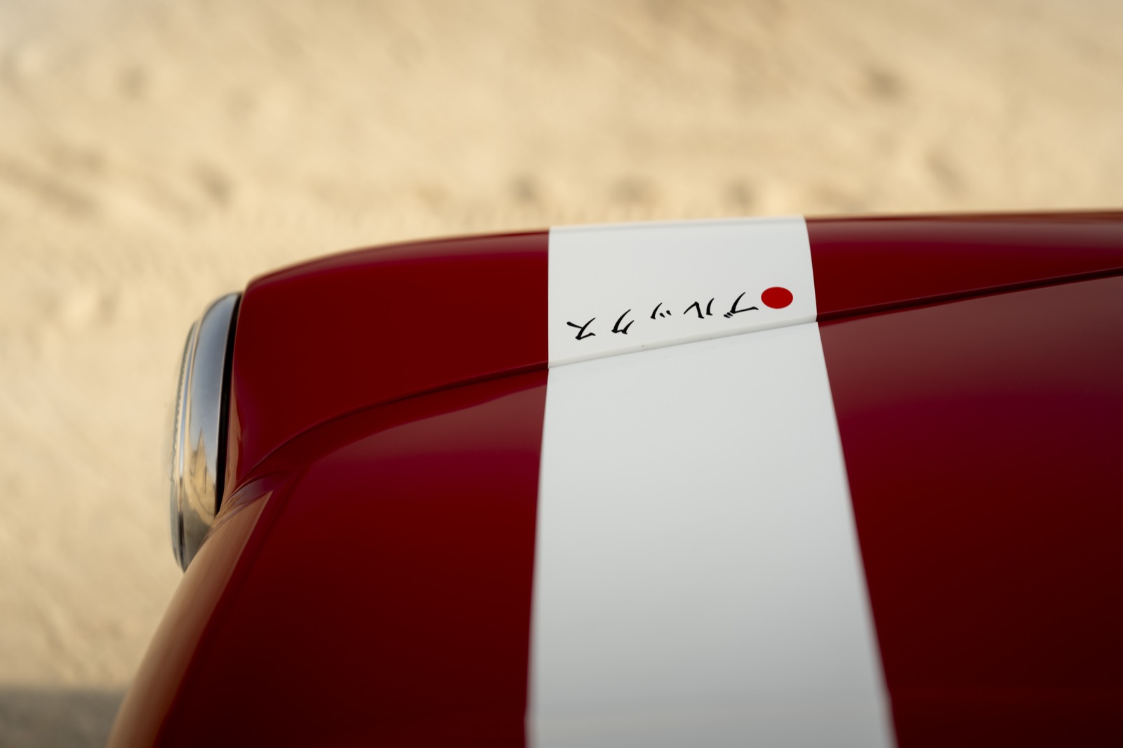 A close-up of a red container topped with a white band, resting on a sandy surface.