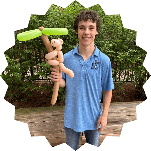 Shayne smiling and holding a balloon palm tree and balloon monkey