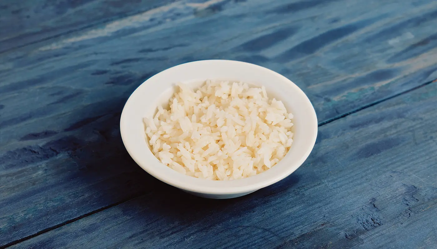 White rice in a white bowl on blue wooden boards.