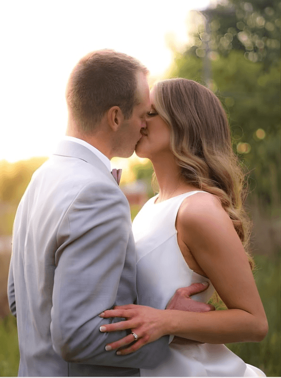 A bride in a white lace wedding dress holds a colorful bouquet of pink, yellow, and orange flowers.
