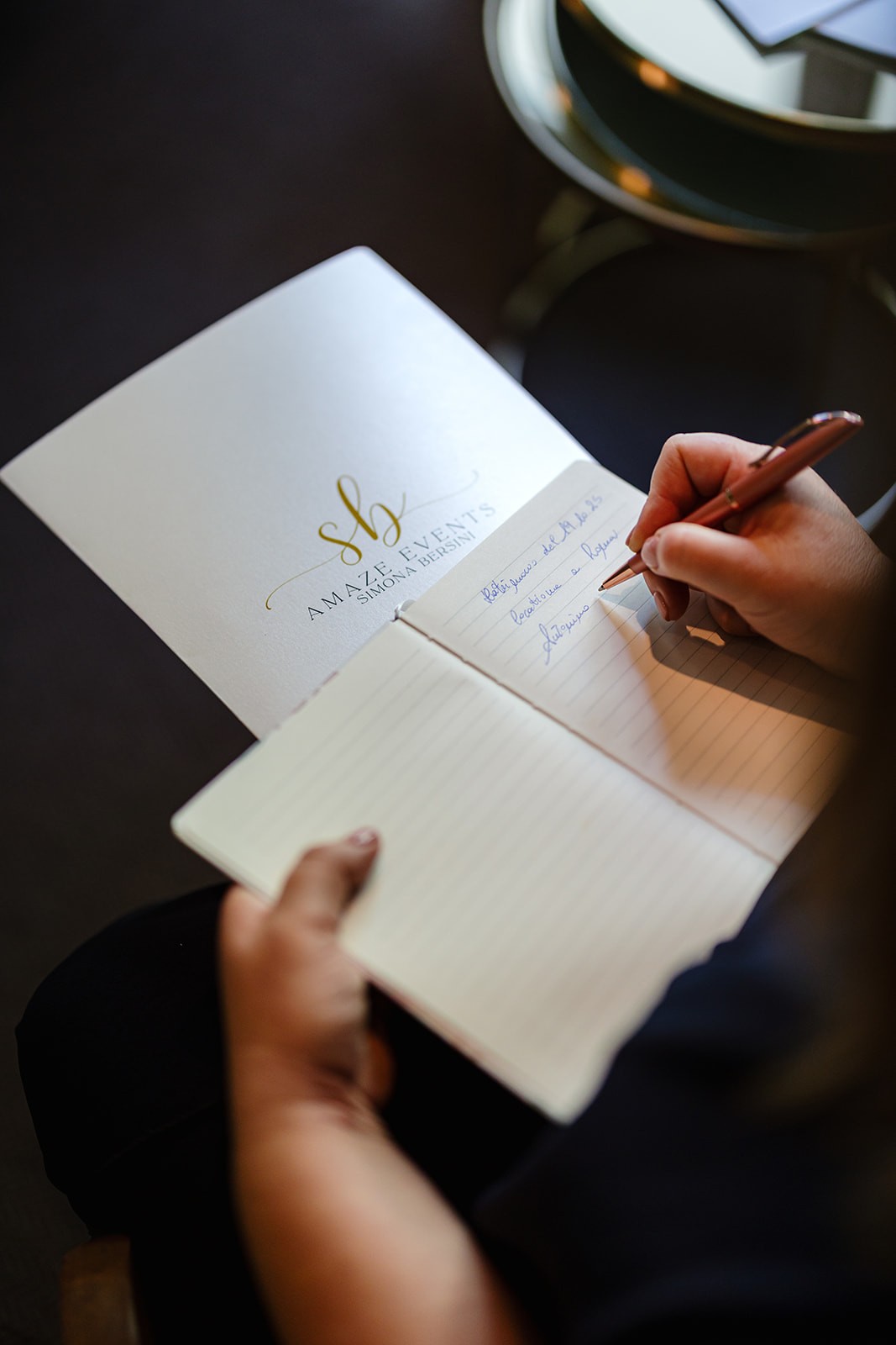 A smiling woman with her arms crossed, standing against a dark green background. She has long, dark hair.