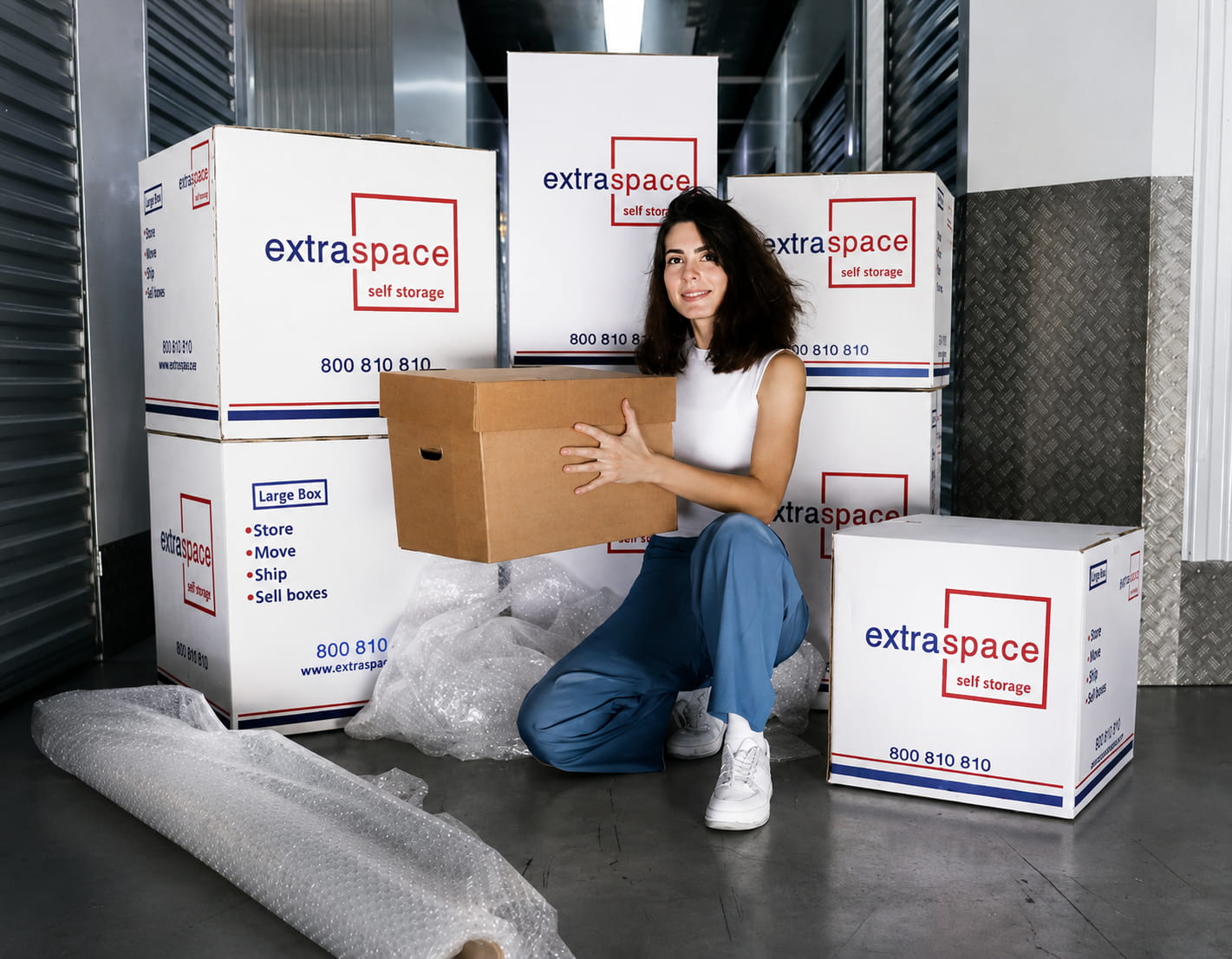Woman holding a moving box among Extra Space Storage boxes and packing materials in a storage facility.