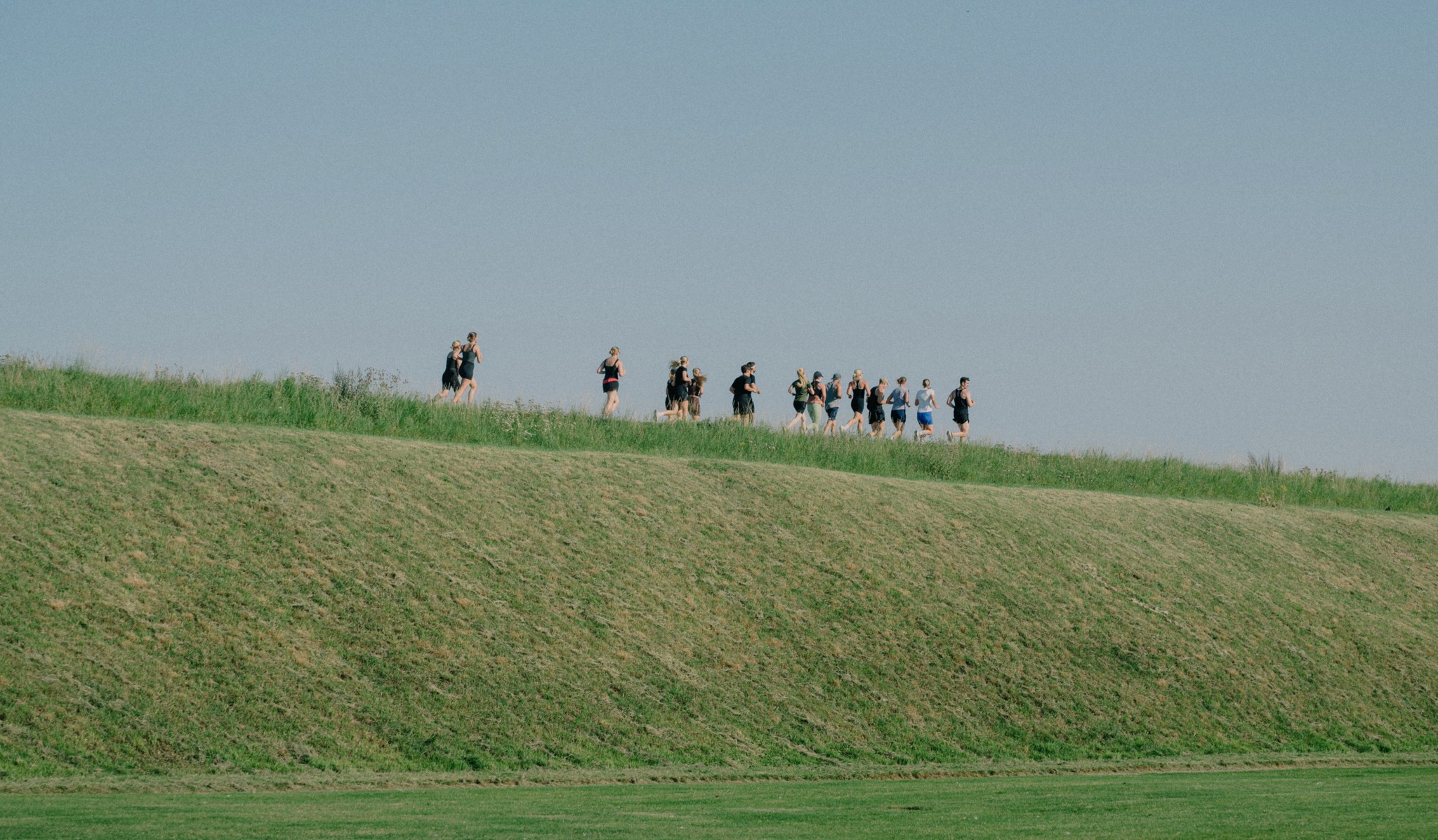 Group of people running on top of a long grassy hill. 