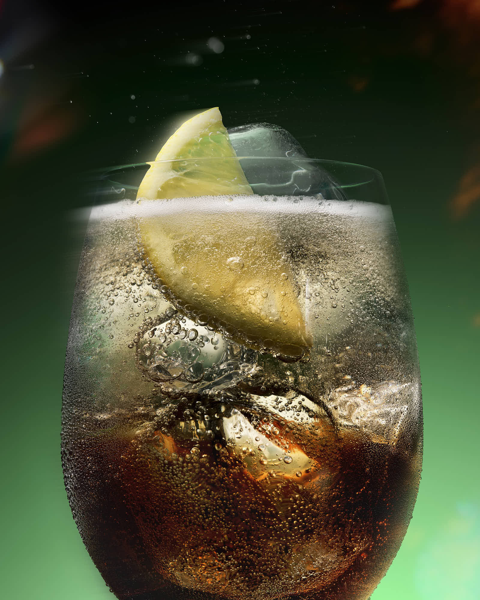 A close-up of a glass filled with a dark fizzy drink, ice cubes, and a slice of lime on top, against a green background.
