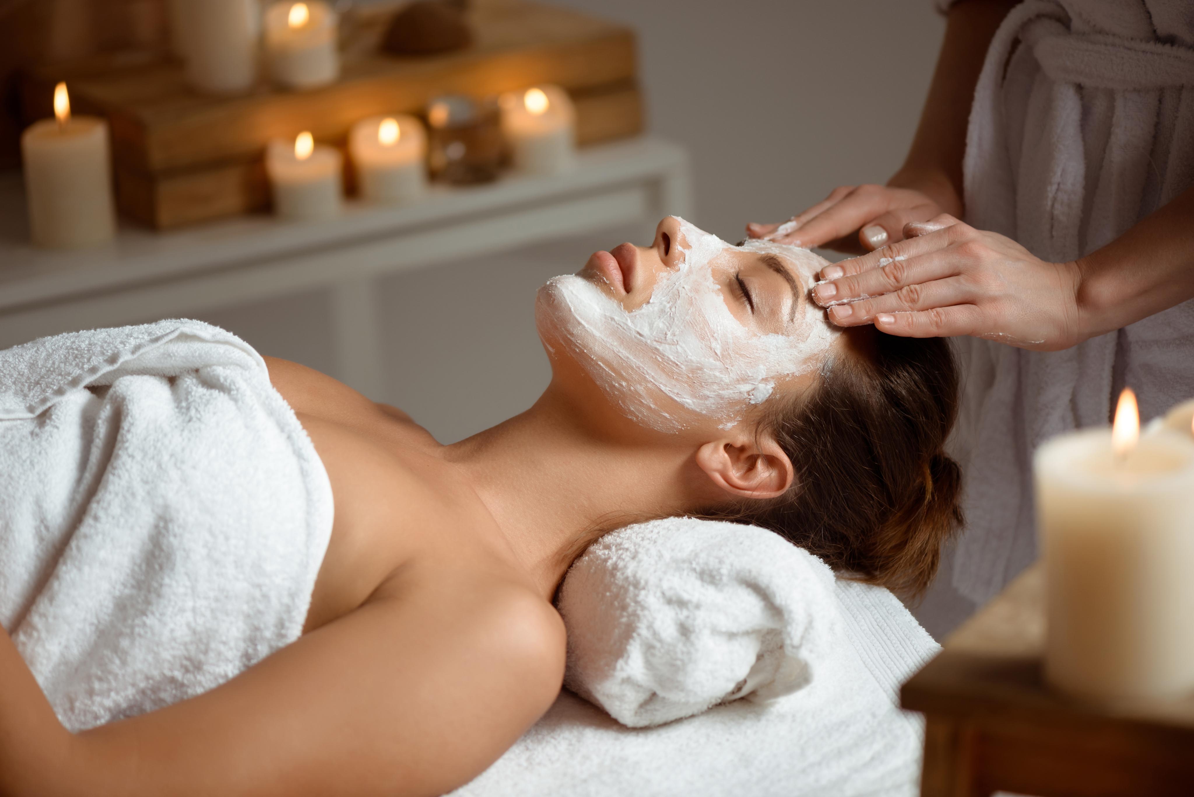 A woman at a spa getting a facial treatment surrounded by candles