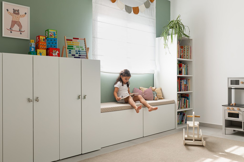 ילדה קוראת ספר על ספסל מעוצב בחדר ילדים.