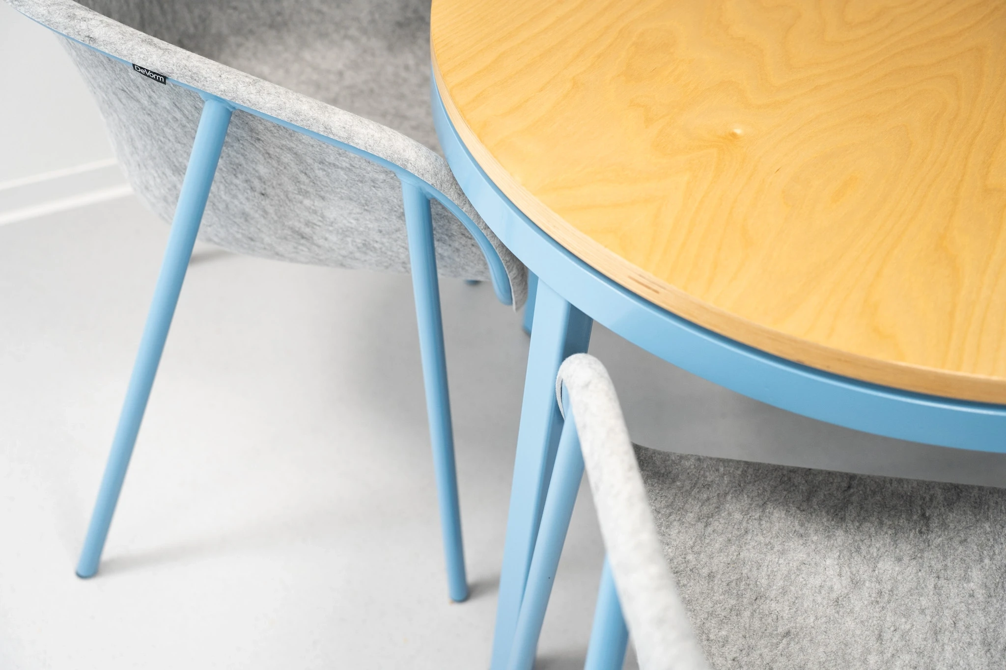 Detail of a round birch table with a light blue frame and matching grey felt shell chairs on blue legs at NFON.