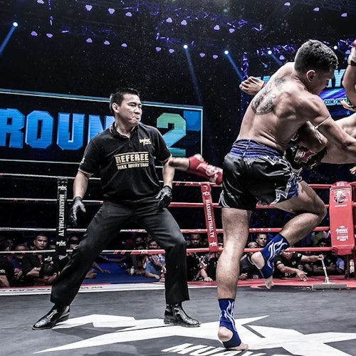 两名泰拳拳手在擂台上进行对打，同时裁判在旁观战。背景中可以看到“回合二”的标志。