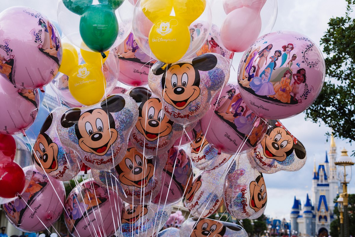 A bunch of Mickey Mouse and Disney princess balloons at Magic Kingdom, with Cinderella Castle in the distance