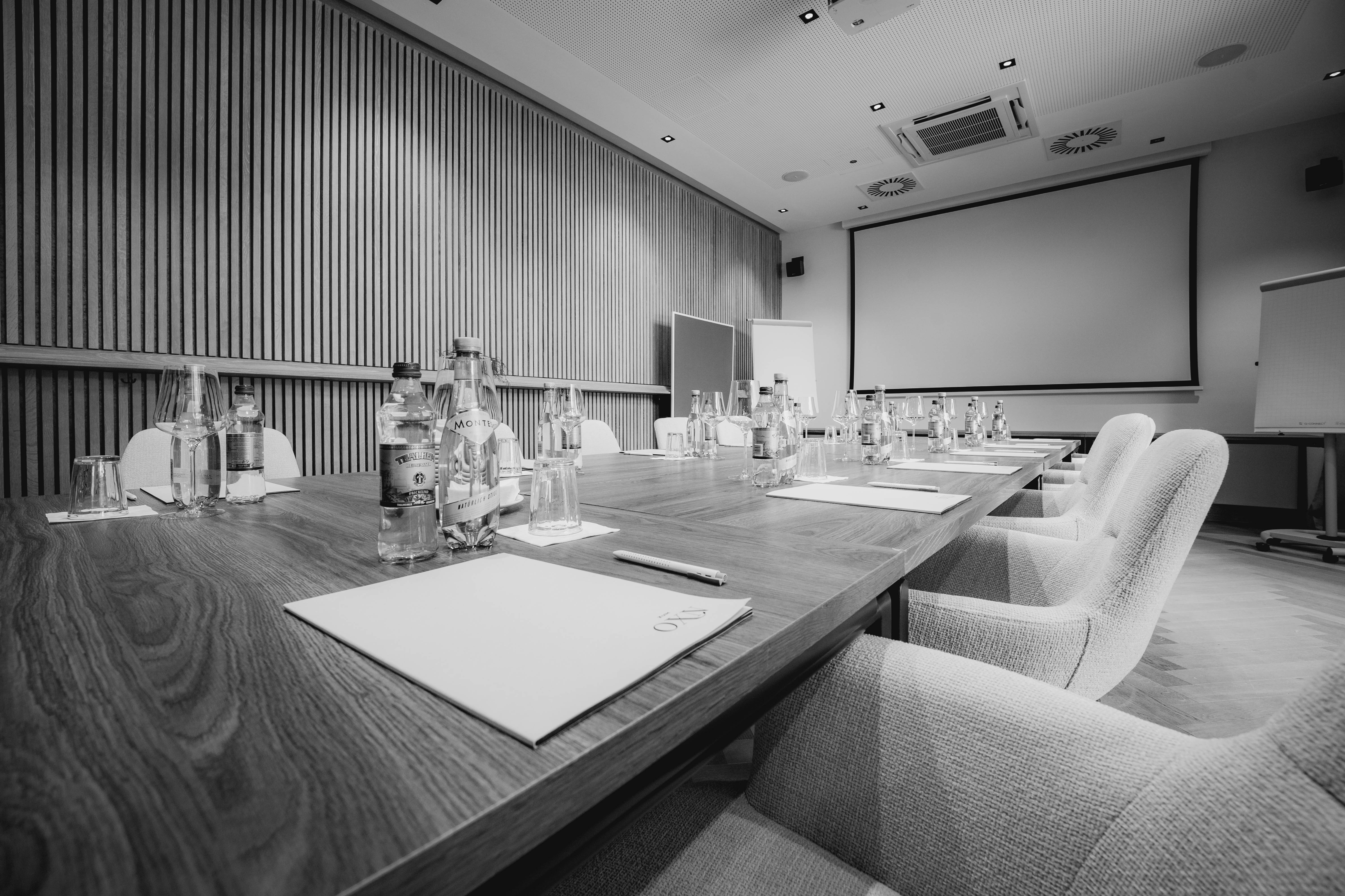 A modern classroom in black and white, featuring desks, a large screen, and windows with natural light.