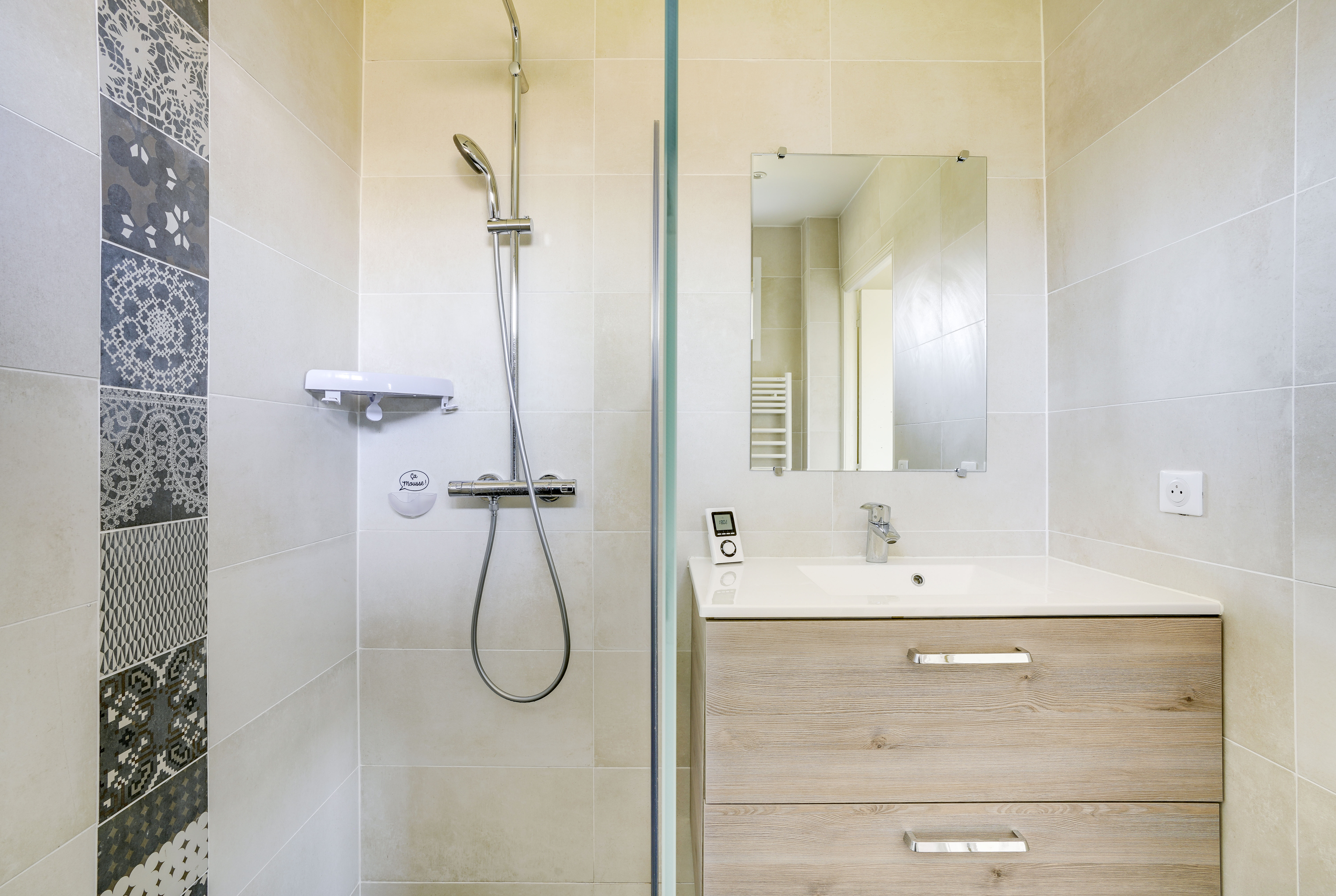 Transformation salle de bains Paris Est avec douche italienne, carreaux décoratifs et meuble-lavabo bois avec évier blanc, rénovation complète.