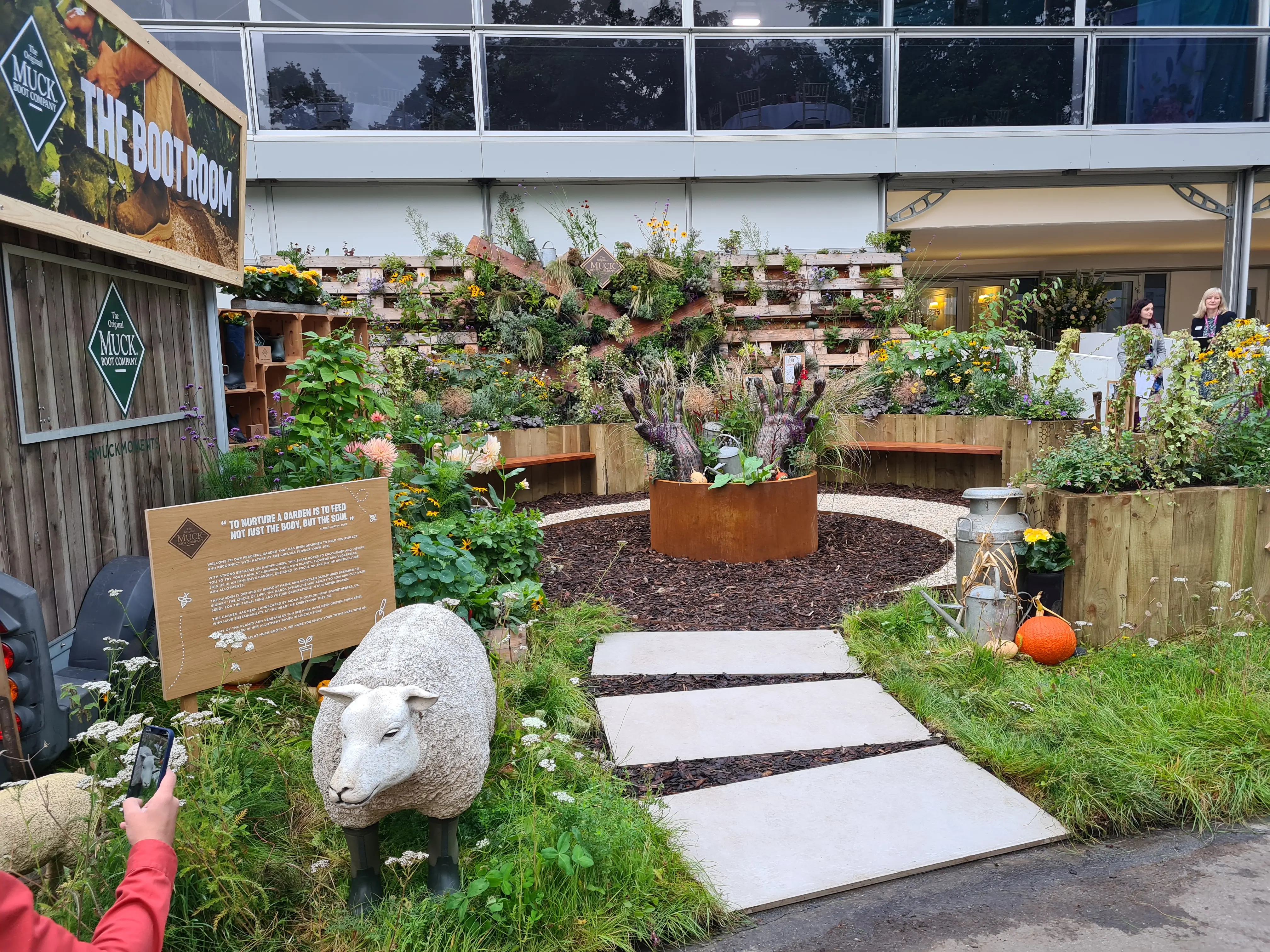 A lush garden with benches, pathways, and colorful flowers, surrounded by greenery and a rustic shed.