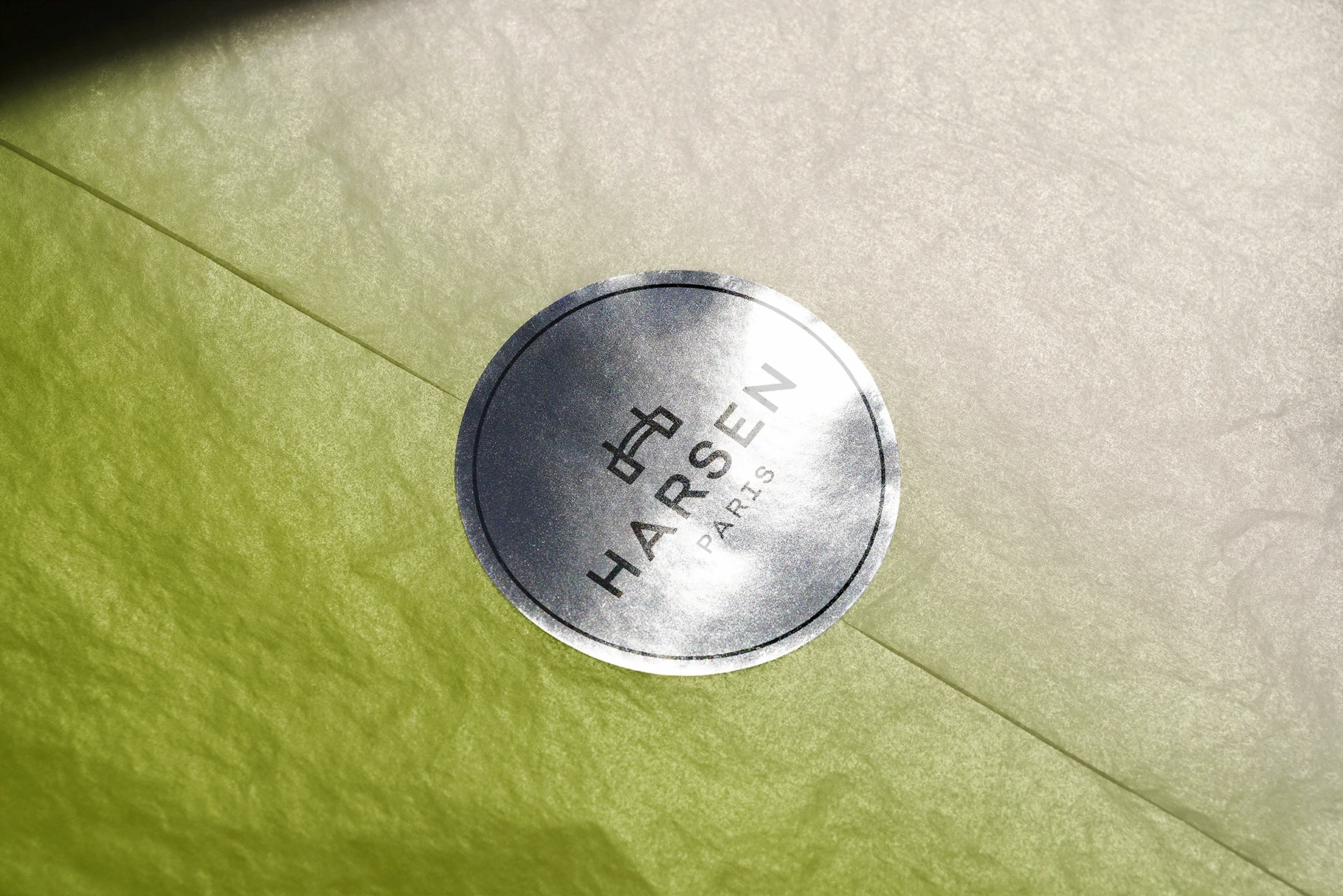 Silver foil sticker mockup with a logo, sealing a light green paper wrap.