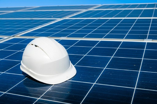 A white hard hat placed on a solar panel, with a clear blue sky in the background.