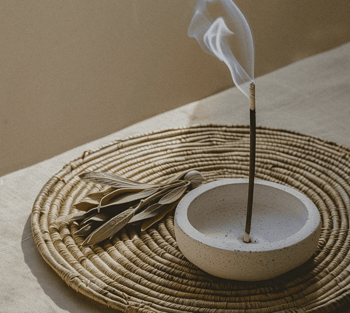 Incense burning and releasing smoke from a stone bowl, accompanied by green leaves, all resting on a unique, patterned mat.