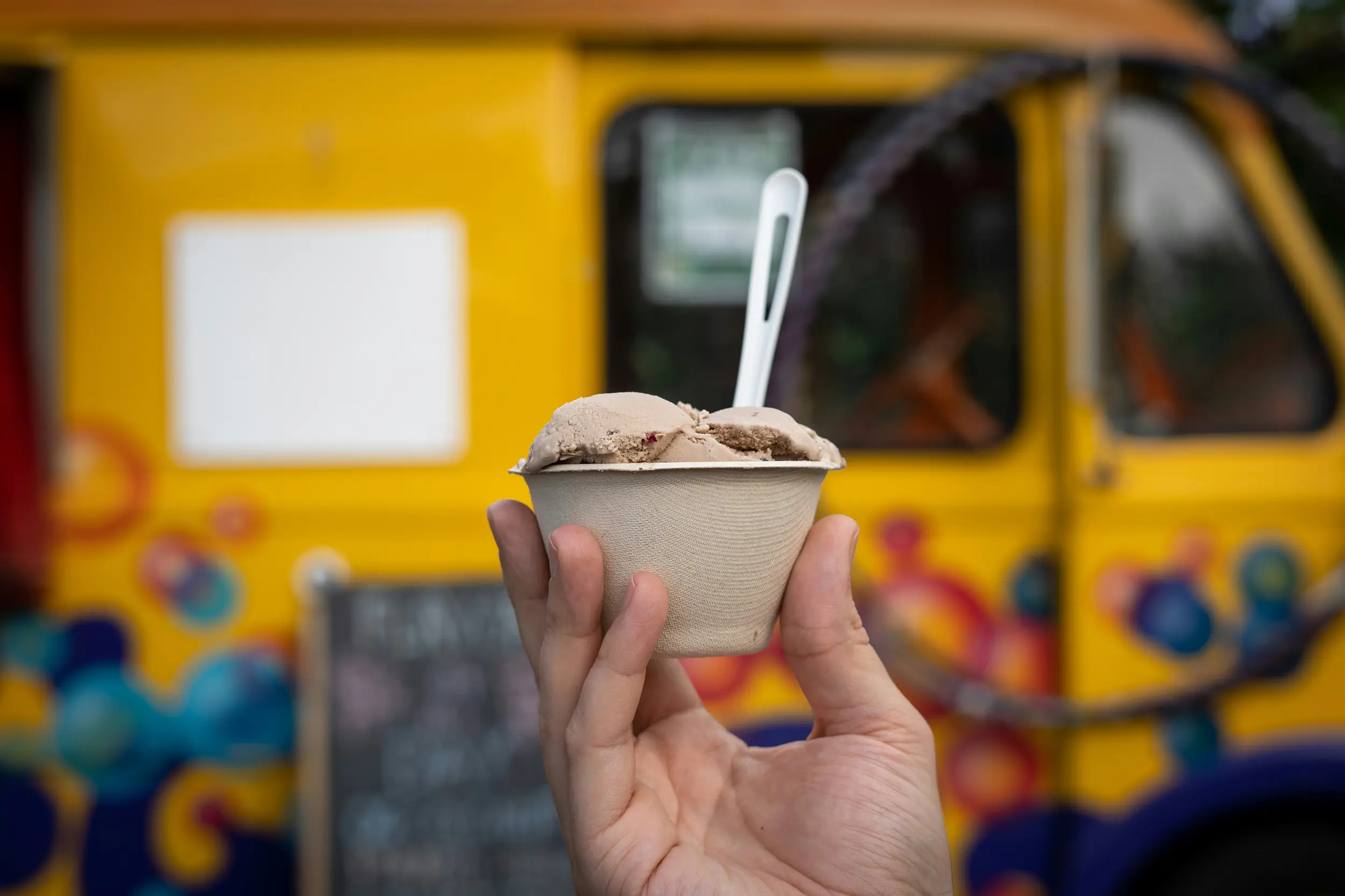 Eine Hand hält einen Becher mit Eis vor dem Eis Carlo Eismobil