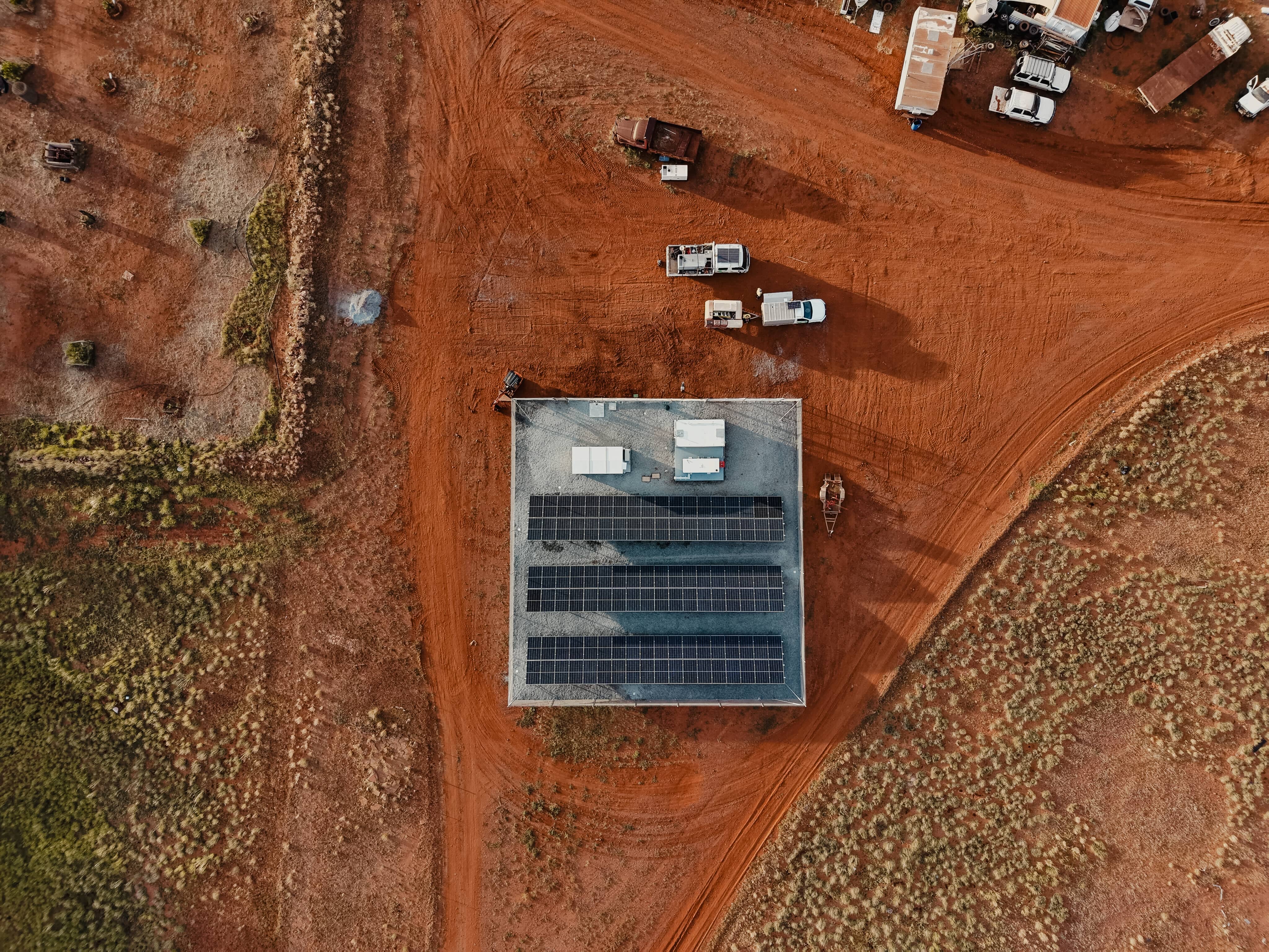 Aerial view of solar panels on a building in a remote, red-dirt Australian landscape with vehicles and infrastructure.