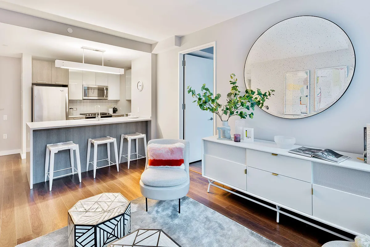 A modern living room showcasing a white kitchen and a decorative round mirror above a console table.