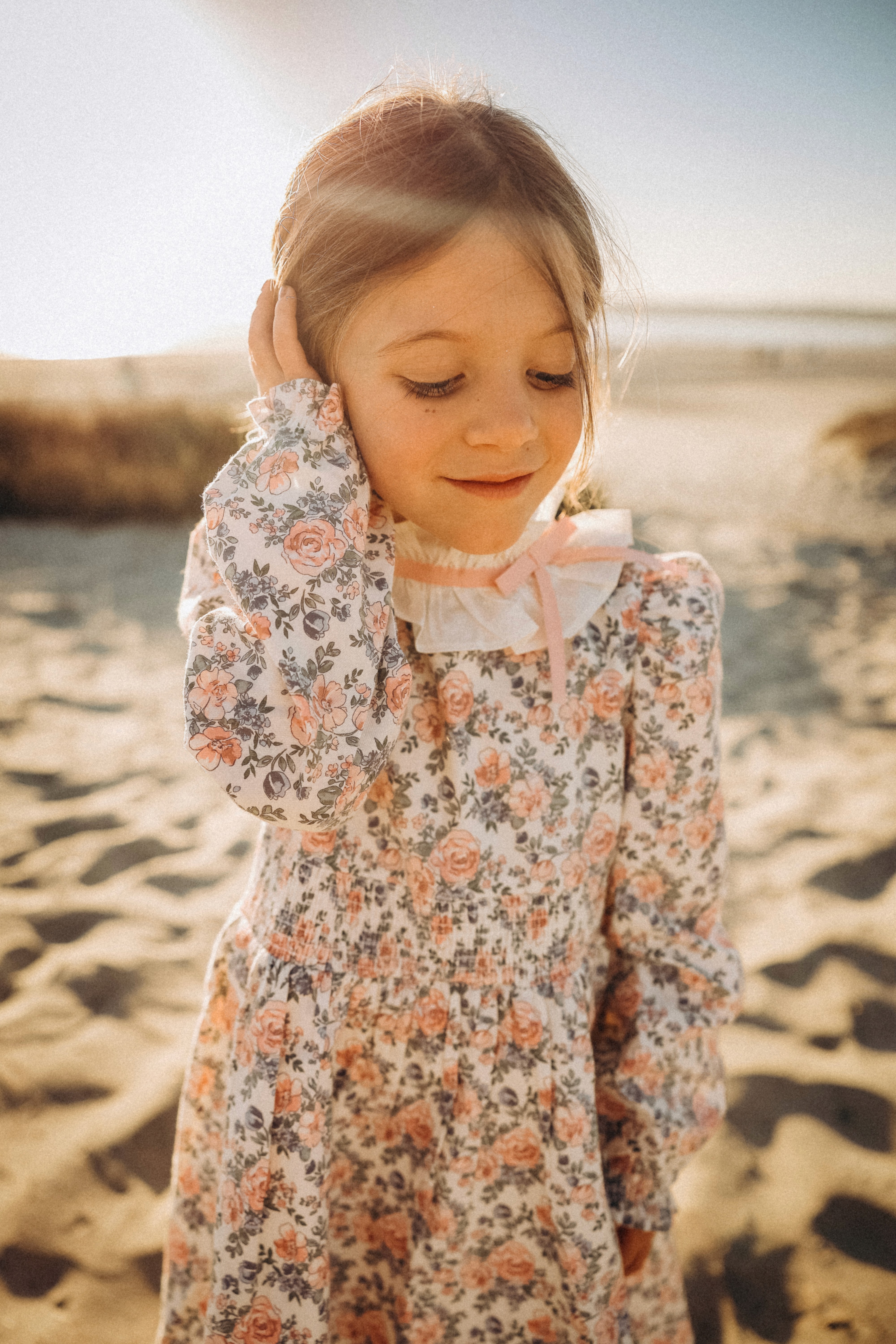 Little girl smiling softly in golden light at the beach during a lifestyle session.