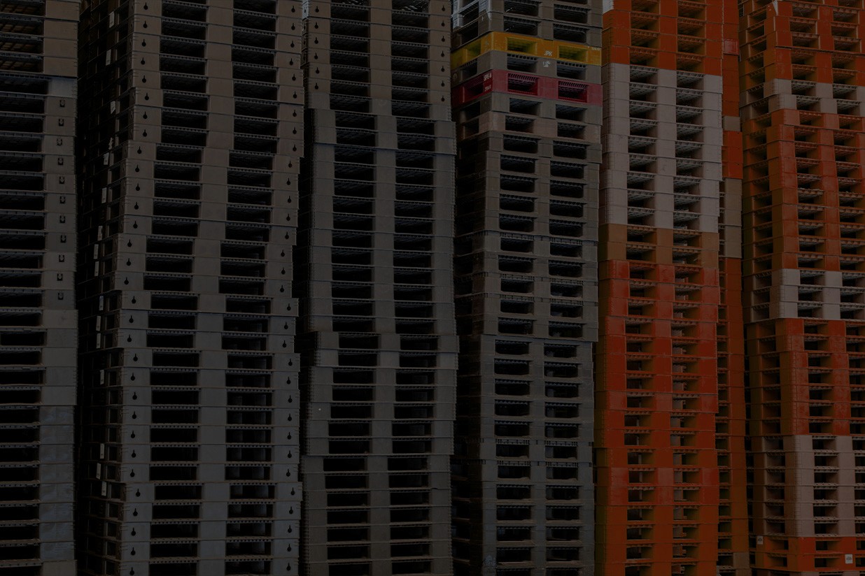 Many black, grey and orange platic pallets stacked on top of each other