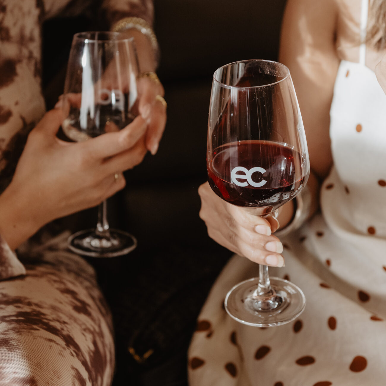 Close-up of two people clinking wine glasses, one glass etched with the eclat logo, at an event