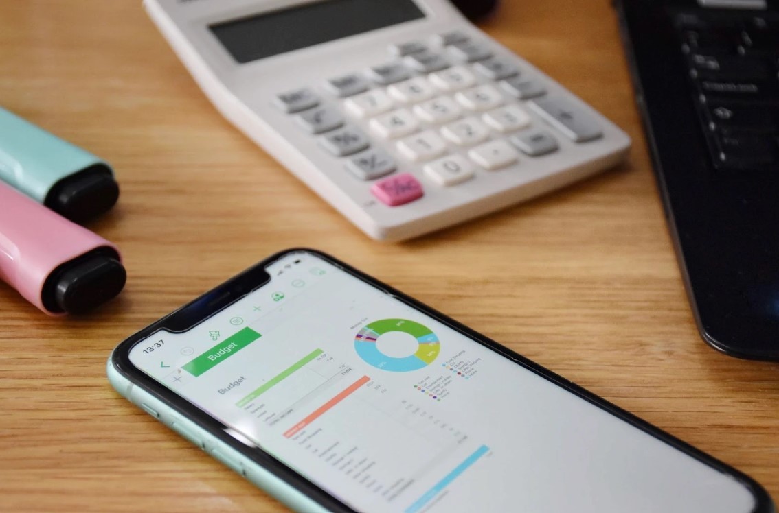 A budgeting app open on a smartphone on a desk next to a calculator and pens.