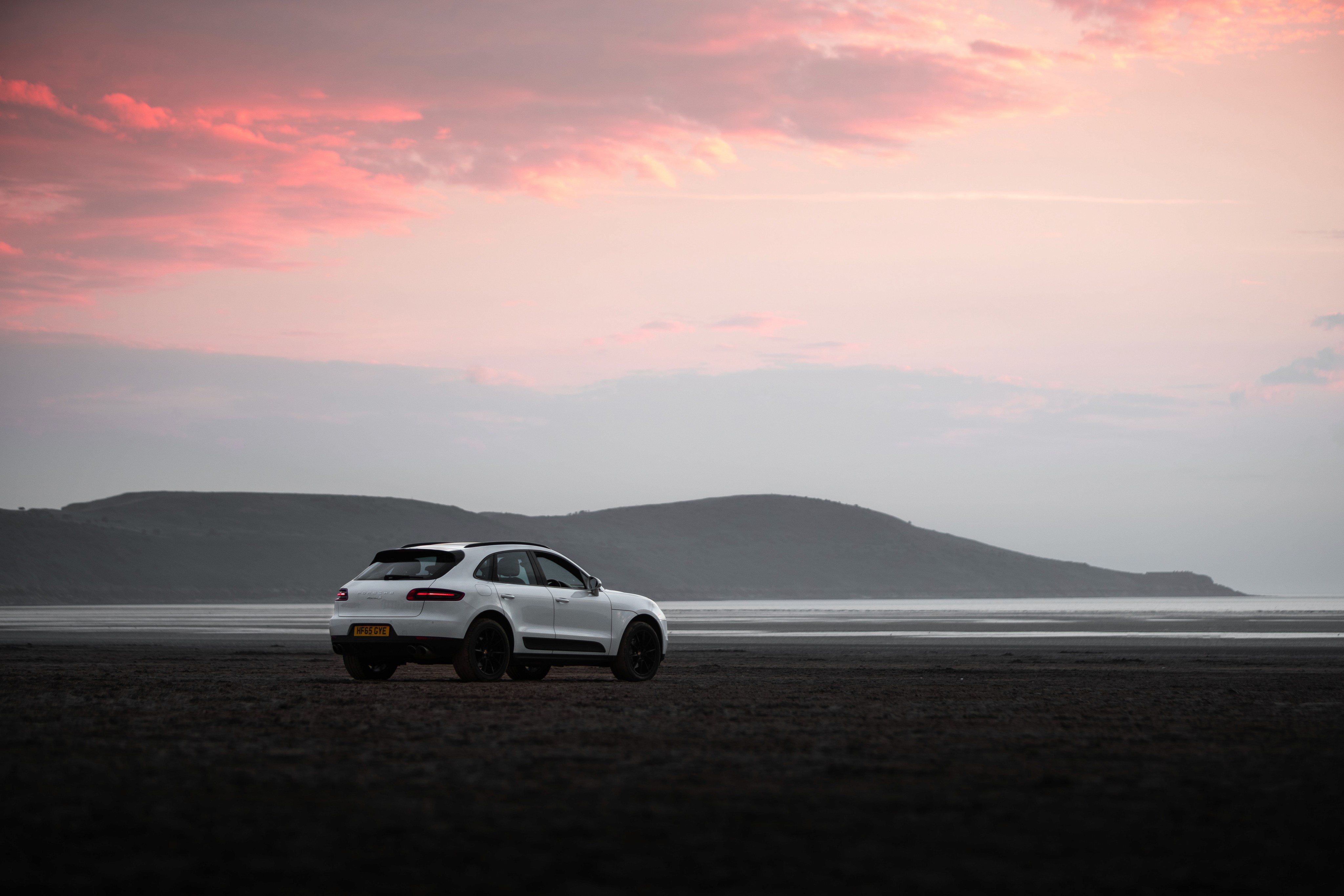 A white porsche driving down a road, with mountain in background at sunset