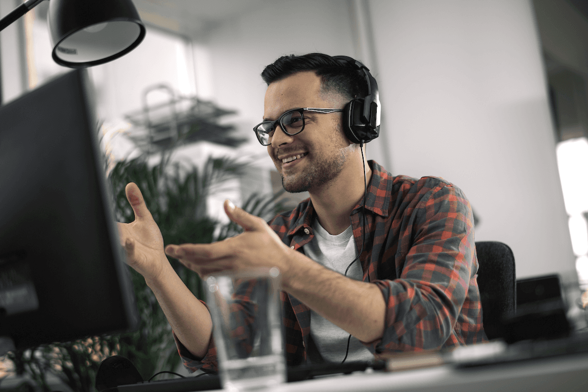 sales enablement app: Smiling man wearing headphones on and doing hand gestures in front of his computer