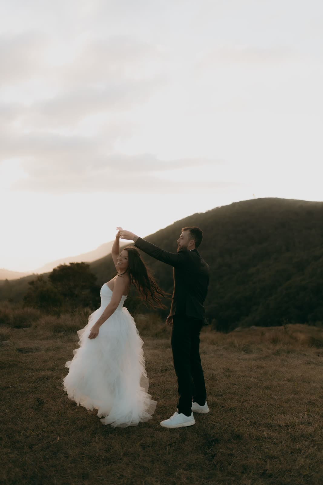 Groom spinning the bride in a white gown on a hillside