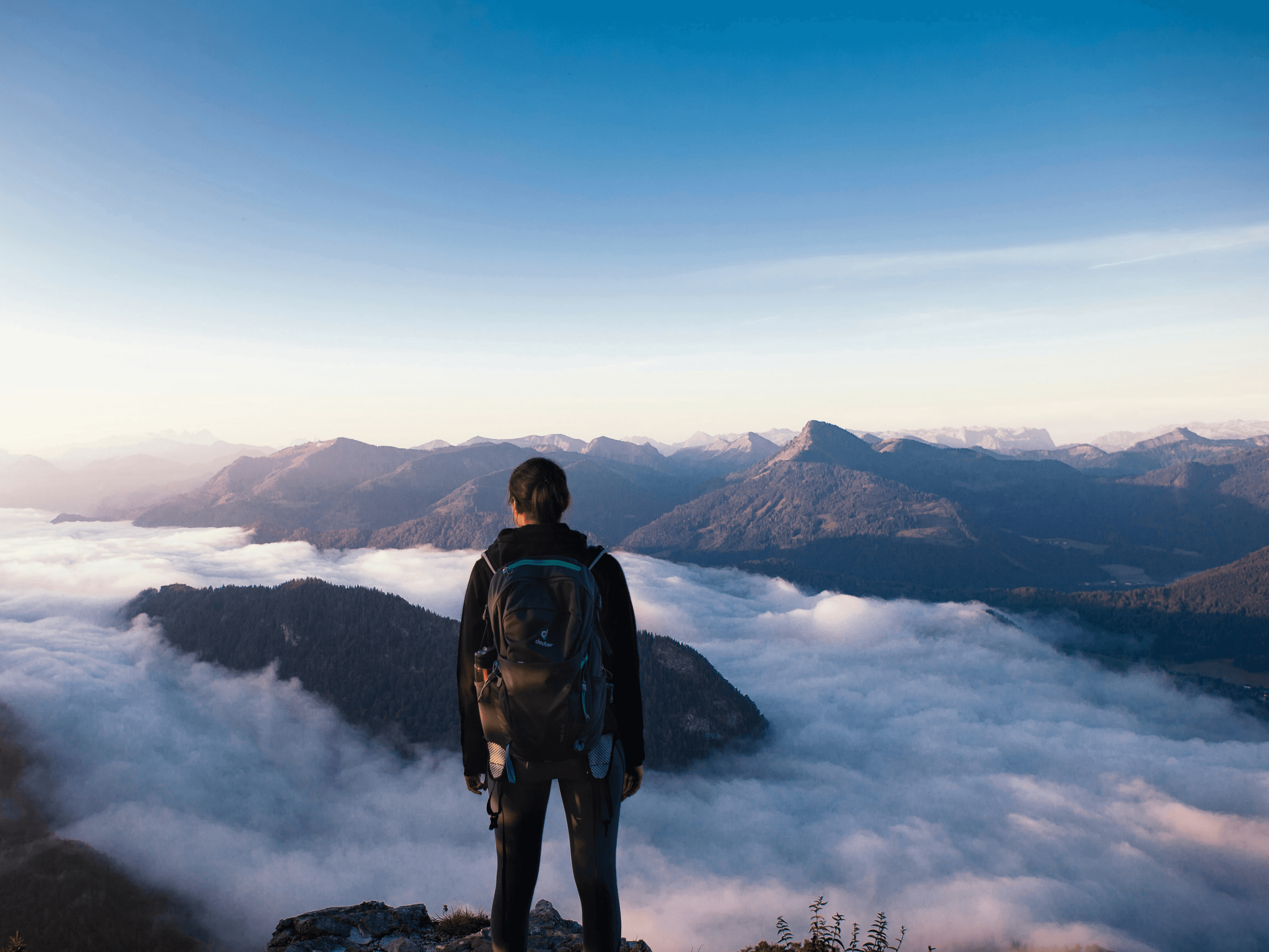 man in black jacket and black pants standing on rock formation looking at the mountains during