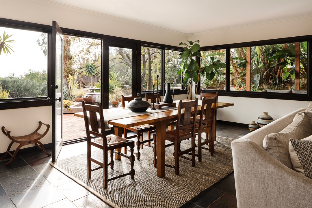 This inviting outdoor retreat features a stone fire-pit, plush sectional seating, and hanging wicker lights, blending earthy tones and natural materials for a cozy, stylish space