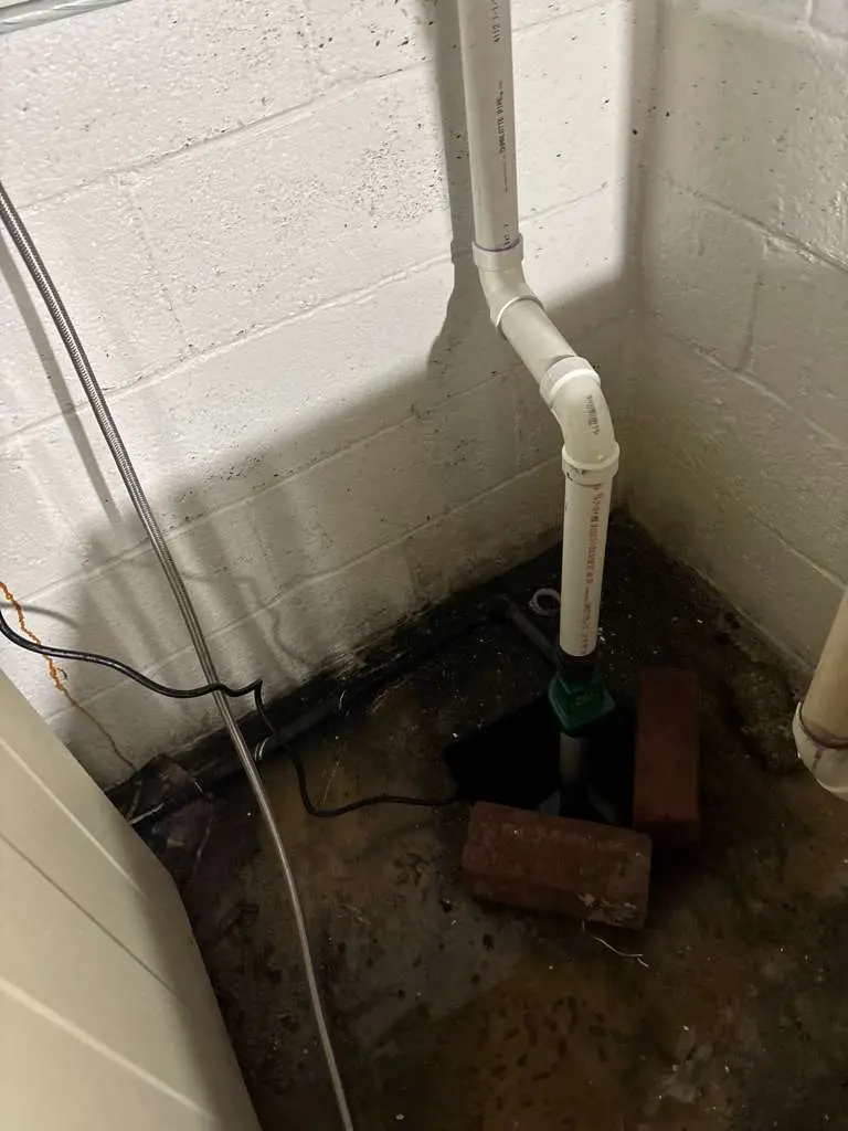 A basement sump pump system with PVC discharge piping inspected during an emergency sump pump repair to prevent basement flooding.