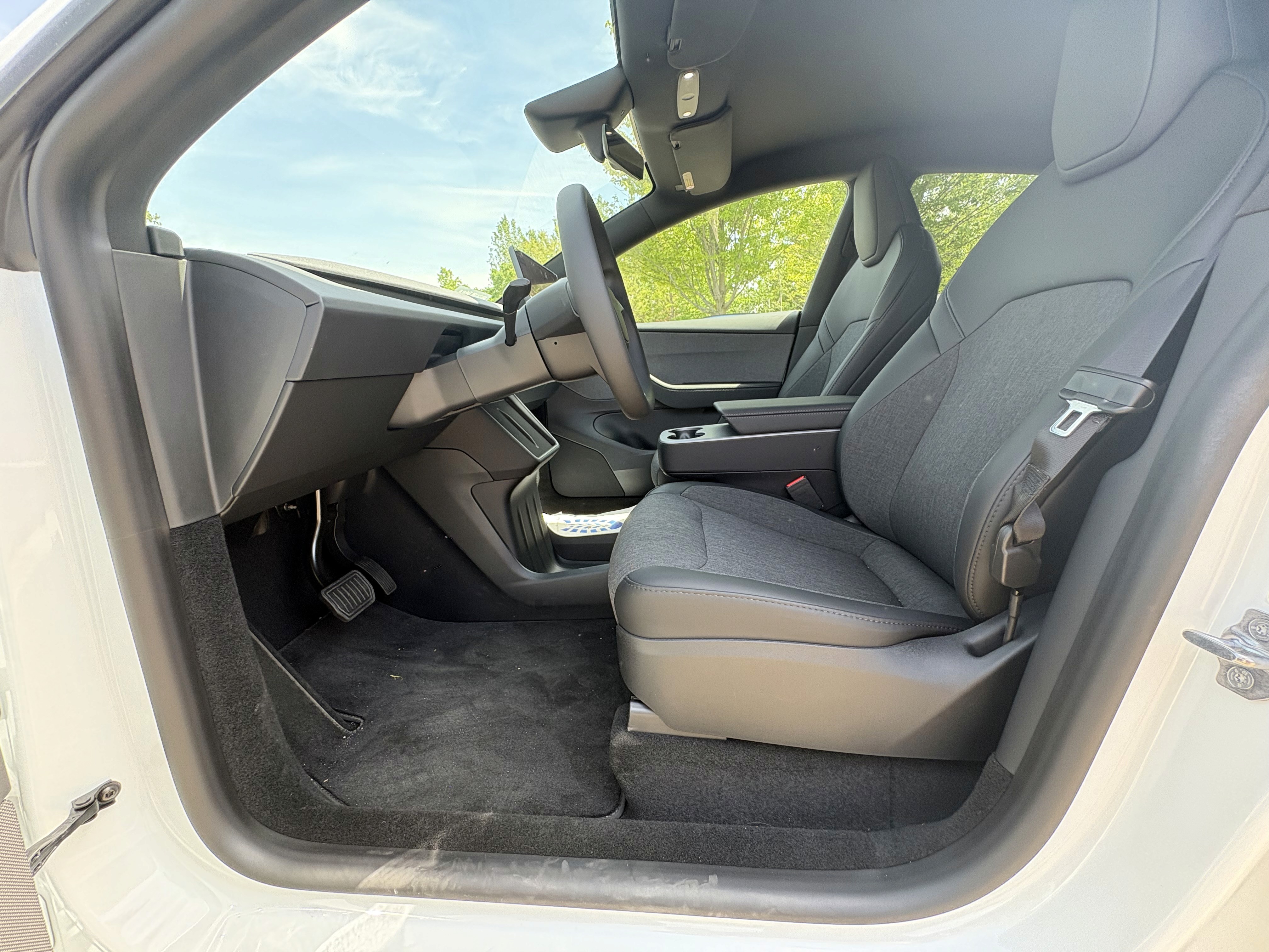 The interior of a Tesla Model Y car, featuring sleek gray seats, a minimalist dashboard, and a steering wheel, highlighted under a bright sky, showcasing automotive design and technology.