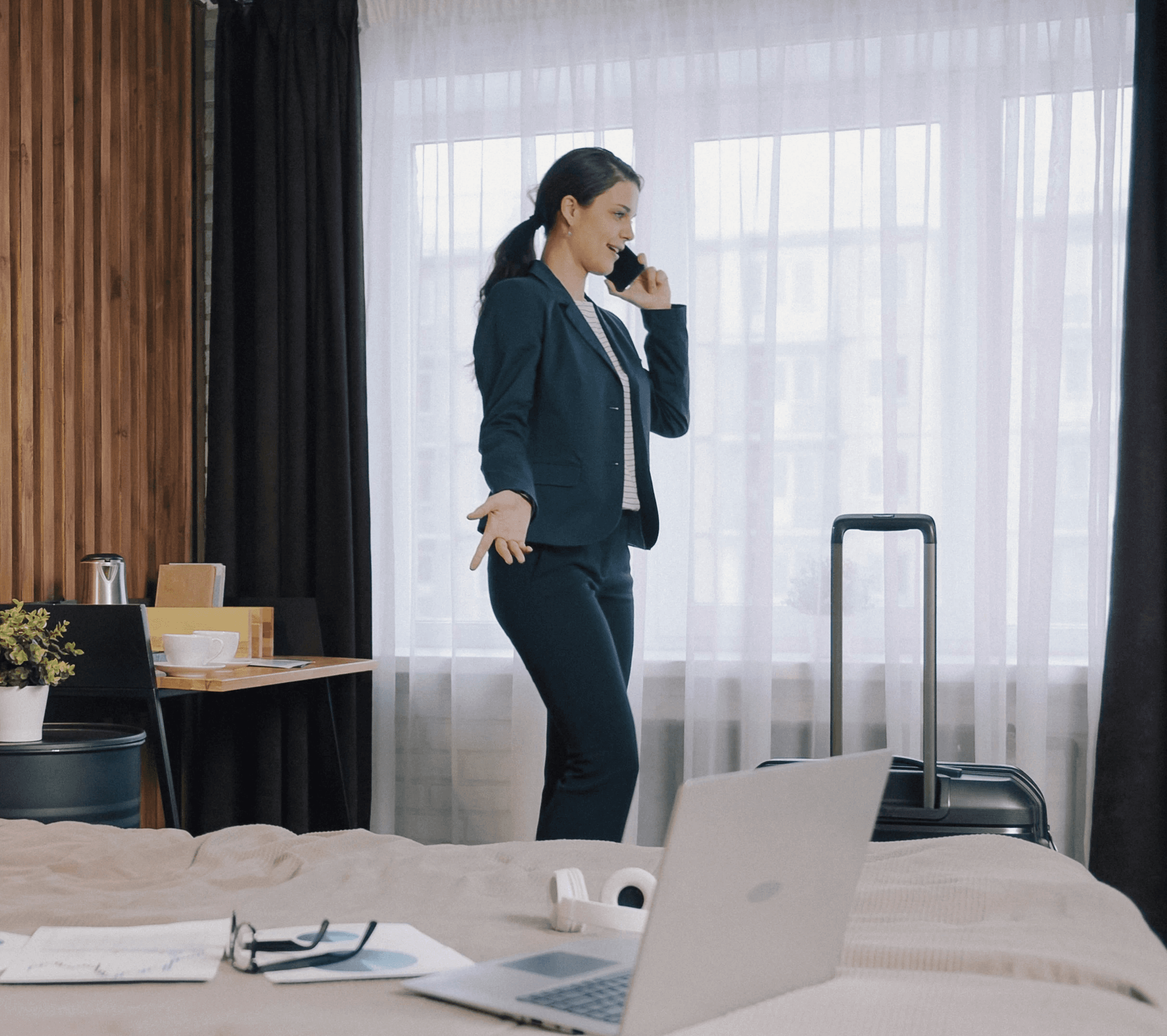 A woman in a dark suit talking on a phone in a hotel room