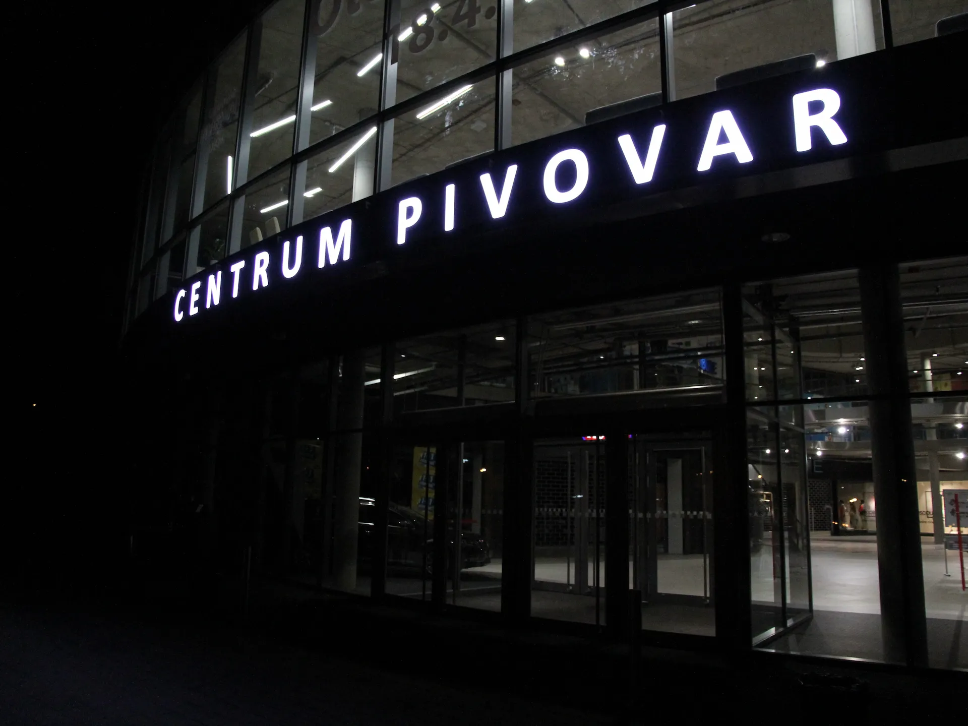 Bílý světelný nápis CENTRUM PIVOVAR na prosklené fasádě obchodního centra v Děčíně v noci